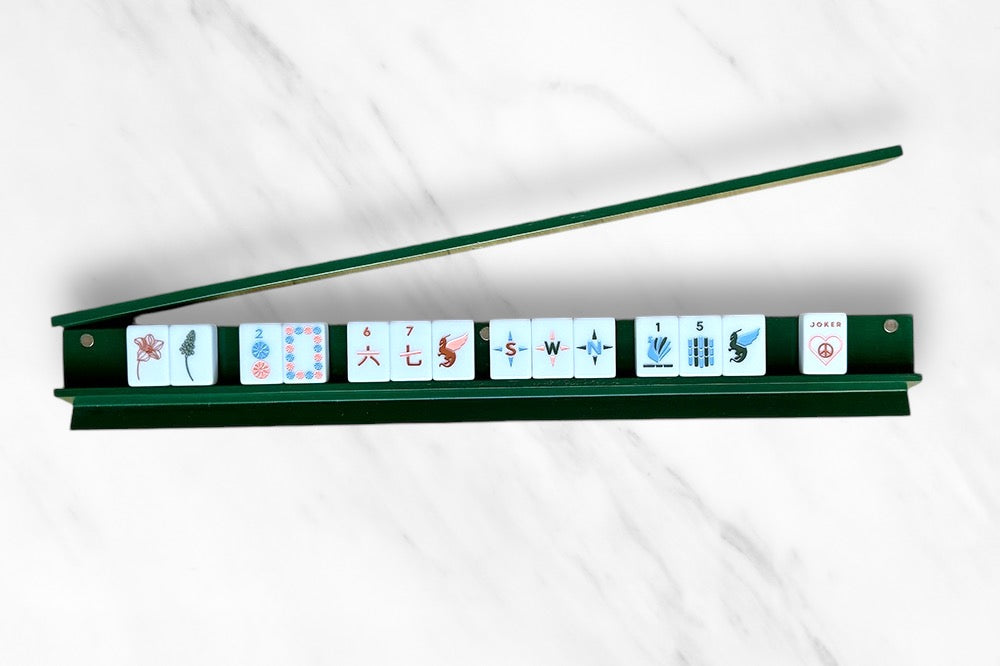 Mahjong rack with tiles and pusher on a marble surface.