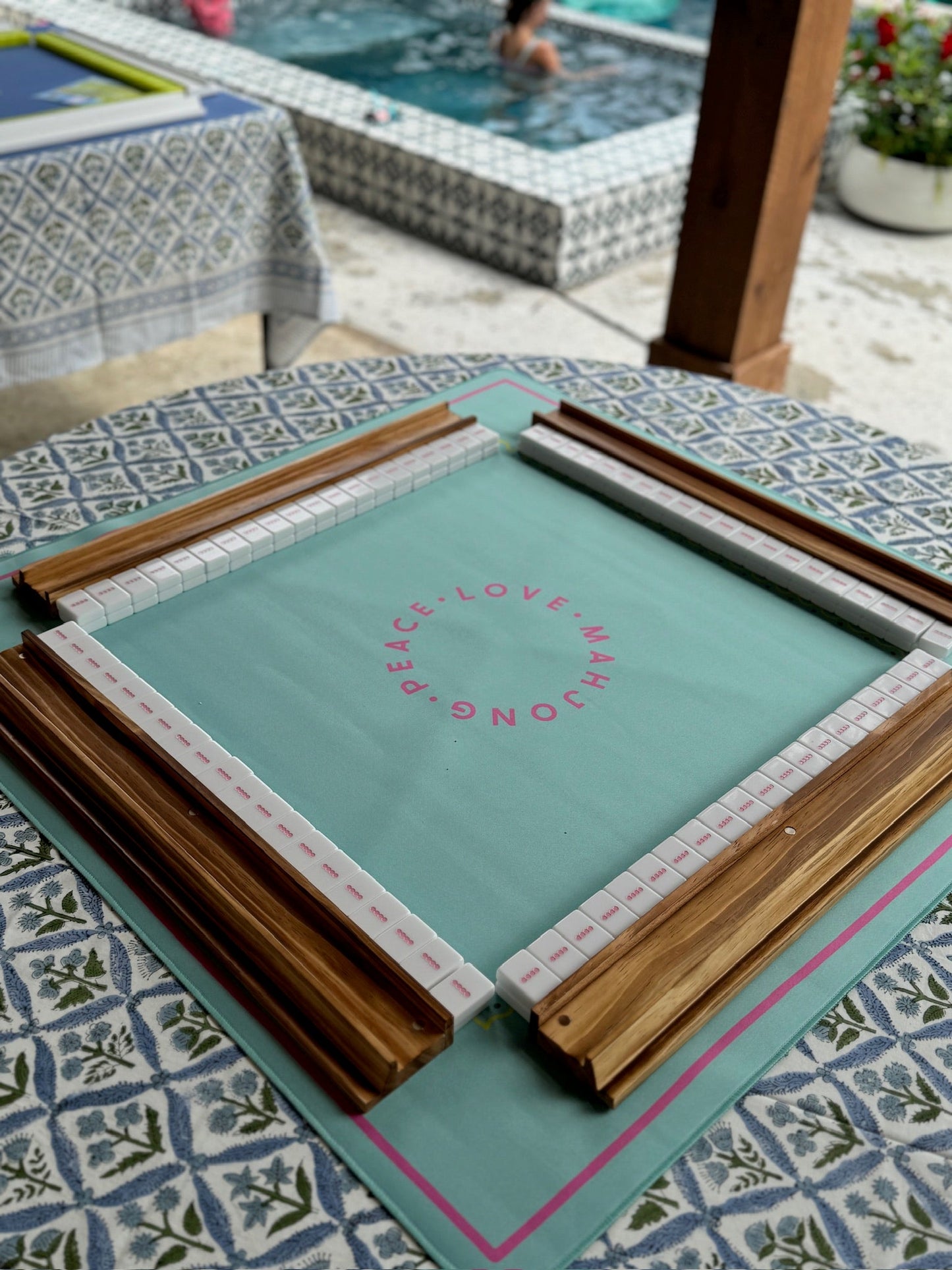 Mahjong racks and pushers set on decorated table near pool.