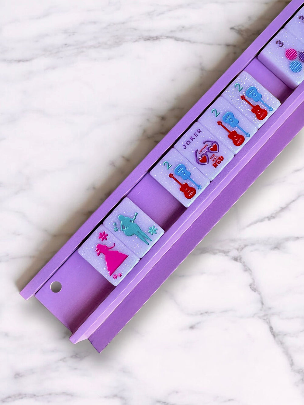 Mahjong rack and pushers in purple, displayed with colorful tiles on a marble surface.
