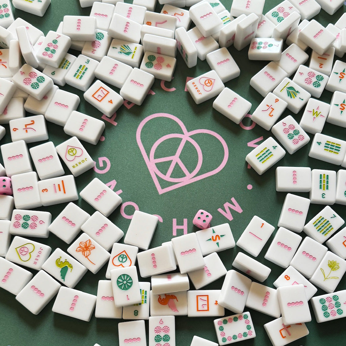 Mahjong set with vibrant white tiles featuring colorful patterns and symbols, arranged on a green surface with a Peace Love Mahjong logo.