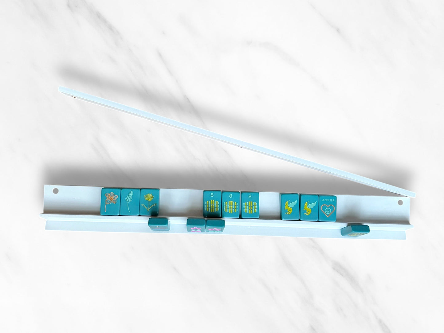 White mahjong racks and pushers set with blue tiles on marble surface.