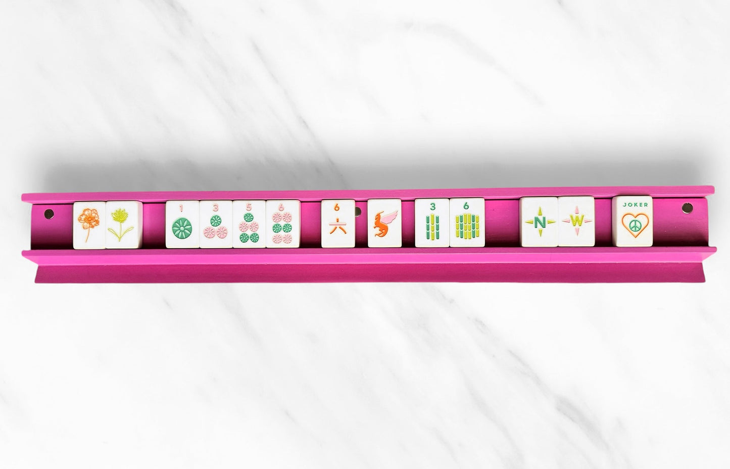 Sleek pink mahjong rack with tiles displayed on a marble surface.